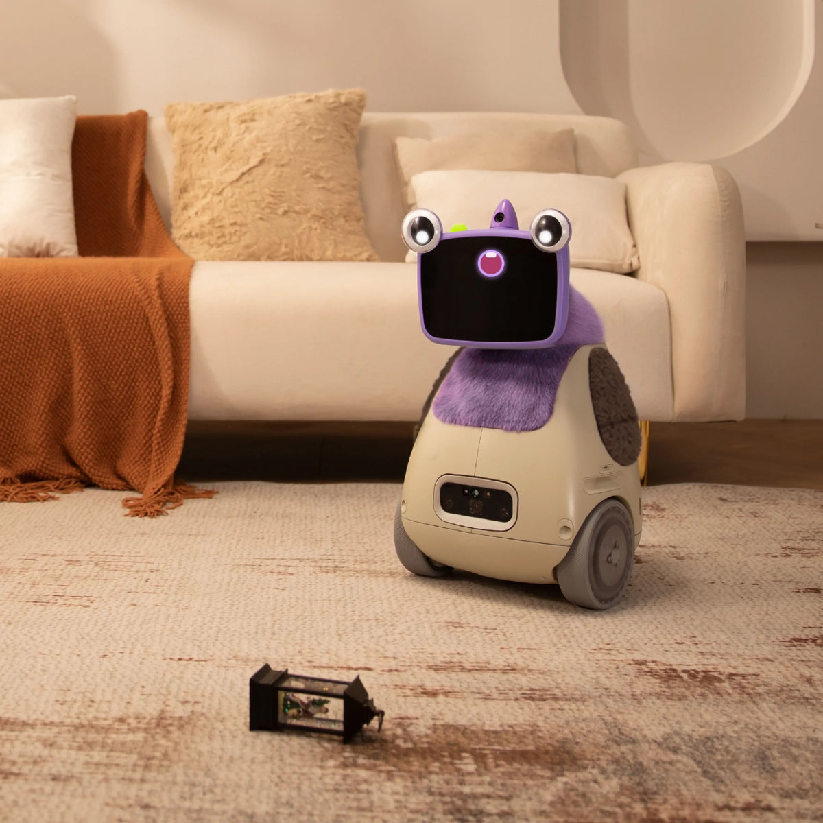 Small wheeled robot with a black screen face and purple collar on a beige rug in a living room.