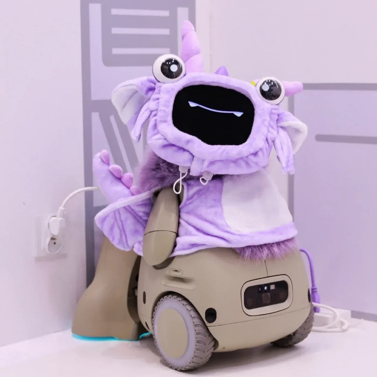 Small wheeled robot with a smiling screen face wearing a plush purple monster costume